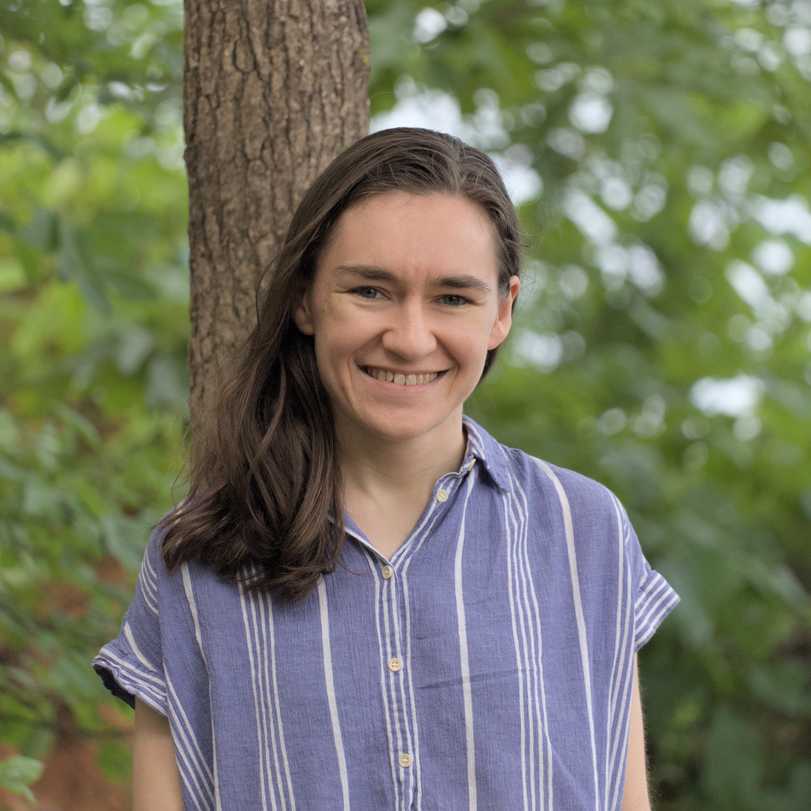Photo of Alayna in a blue shirt standing in front of some trees